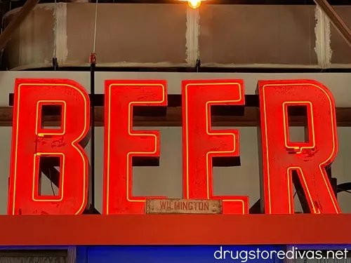 A neon red sign that says BEER in capital letters with a small wooden sign that says WILMINGTON in front of it.
