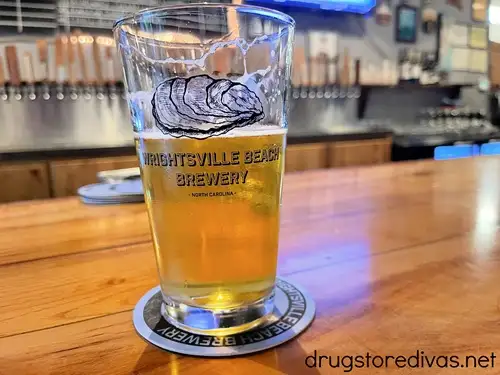A 2/3 filled beer mug in a glass that says "Wrightsville Beach Brewery" on it on a bar with tabs behind it.