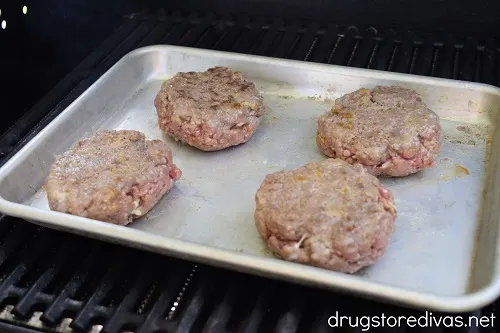 Four burger patties on a pan on a grill.