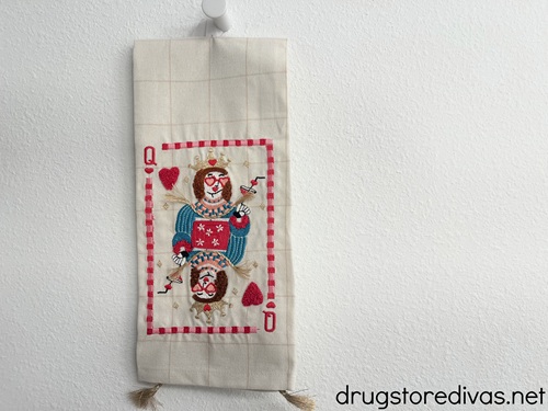 A Queen of hearts playing car design on a white towel that's hanging on a wall.