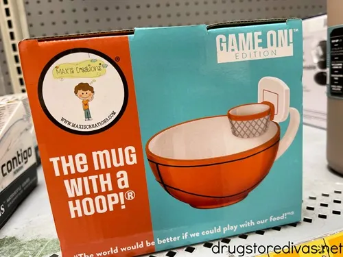 A mug that has a basketball hoop attached in a box on a shelf.