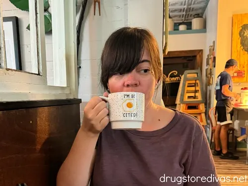 A woman with dark hair in a purple shirt holding a mug that says I'm so egg-cited.
