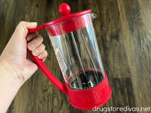 A hand holding a red French press.