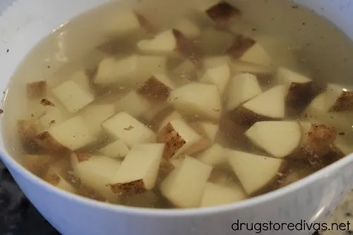 Potato pieces submerged in water in a white bowl.