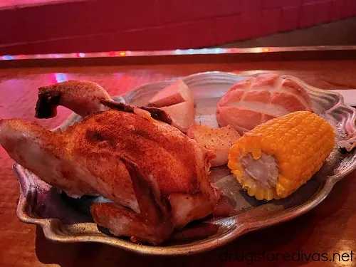 Cornish hen, potatoes, a roll, and corn on the cob on a plate.