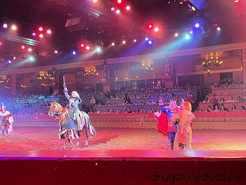 Man on a horse with a sword raised, plus a king and a knight, in the Tournament of Kings arena.