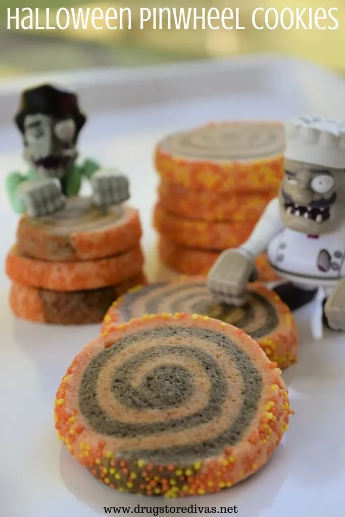 Homemade black and orange swirl pinwheel cookies, with two Halloween zombie toys, on a tray and the words "Halloween Pinwheel Cookies" digitally written on top.