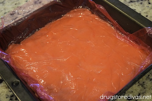 Orange cookie dough, covered in plastic wrap, in an 8x8 pan.