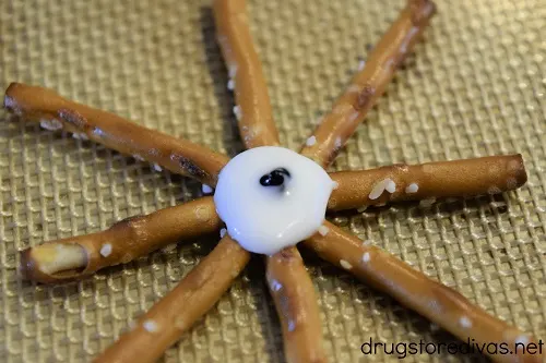 Black dot of decorating gel in the middle of a white almond bark circle that's in the middle of eight pretzels.