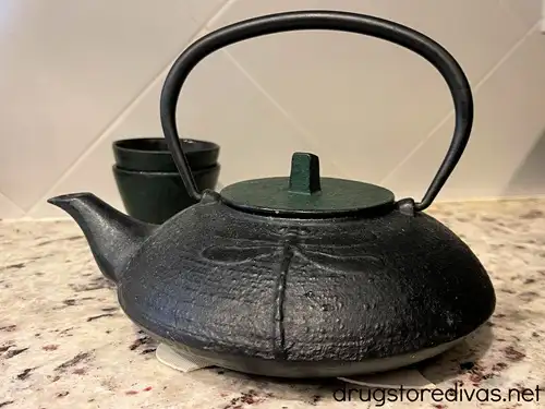 A black Japanese tea kettle with a green lid next and two green Japanese tea mugs behind it.