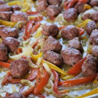 Sausage and peppers on a sheet pan with the words 