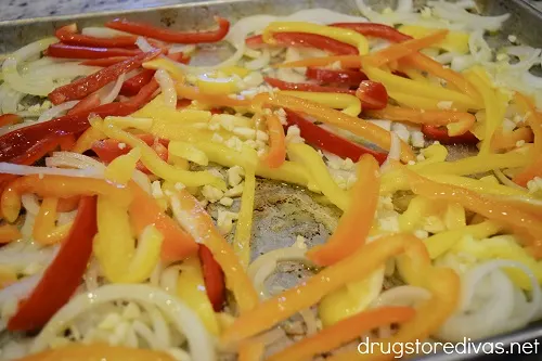 Sliced onions, peppers, and garlic, drizzled with olive oil, on a sheet pan.