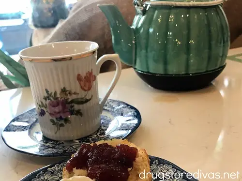 A tea kettle, tea cup, and pastry with jam on a place.