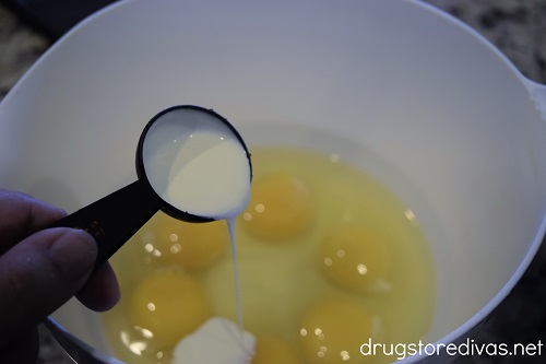 Heavy cream pouring into a bowl with six eggs in it.