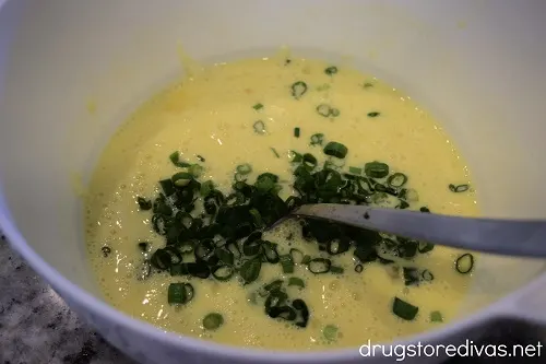 Green onion on top of an egg mixture in a white bowl with a spoon in it.
