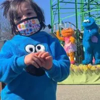 Kid in a Cookie Monster sweatshirt and mask with Cookie Monster and another muppet behind him with the words 