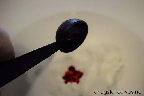 Food coloring being poured into Greek yogurt in a bowl.