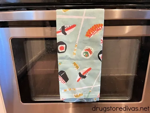A kitchen towel with drawn sushi on it hanging on an oven.