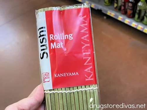 A hand holding a sushi rolling mat in a package in a store.