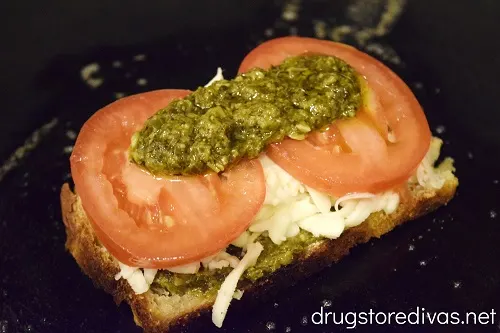 Pesto, tomato, and cheese on a piece of bread in a pan.