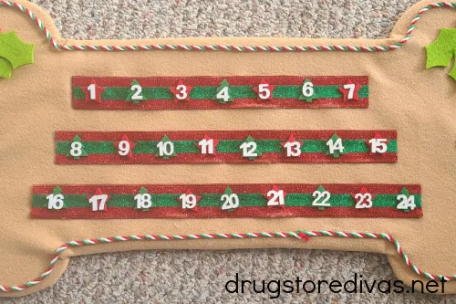 Numbers 1 to 24 glued onto red and green ribbon on a DIY Dog Treat Advent Calendar.