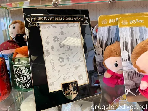 A black picture frame on a shelf that says, "Our House Is The Best" on the top with a Harry Potter logo on the bottom.