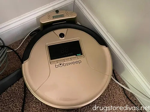A champagne colored, round, robot vacuum in a corner.