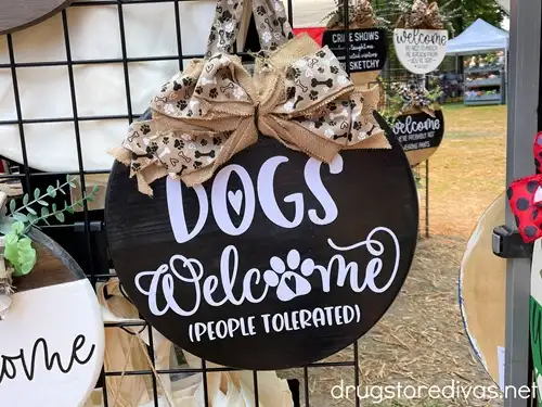 A black, round door sign that says "Dogs welcome (people tolerated)" on it.