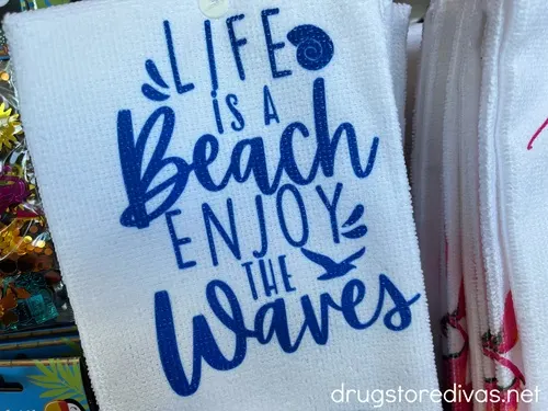 A white kitchen towel that says "Life Is A Beach Enjoy The Waves" on it in blue.