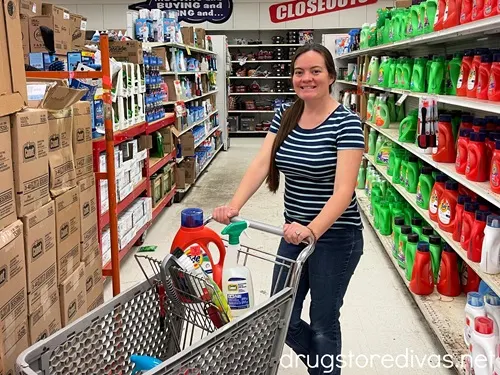 A woman pushing a shopping cart in the laundry aisle of a store.