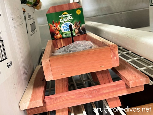 A picnic table shaped squirrel feeder on a shelf in a store.