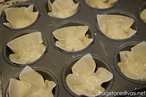 Wonton wrappers in the cavities of a muffin tin.