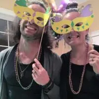 Two people in homemade Mardi Gras masks and beads with the words 