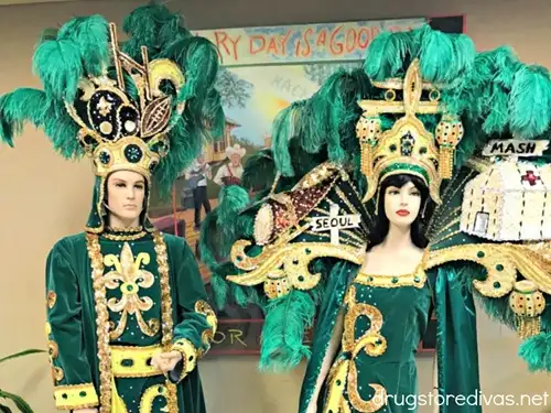 A female and male status dressed up in green Mardi Gras outfits.