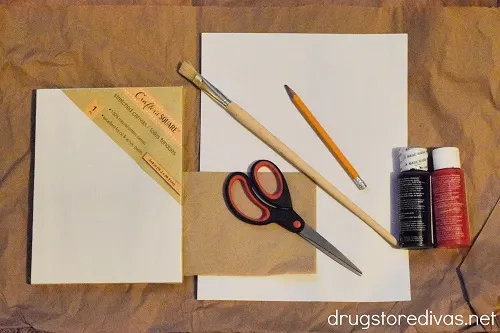 A canvas, paper, paint brush, pencil, black paint, scissors, and a napkin.