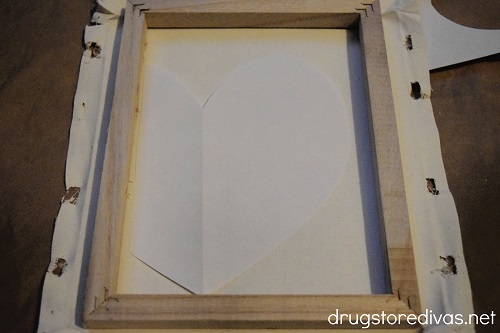 A frame, canvas, and a heart cut from a piece of paper.