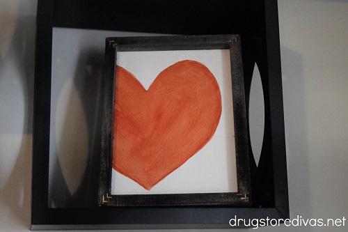 A reverse canvas heart wall art piece displayed on a floating shelf.