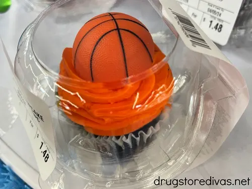 A basketball cupcake in a plastic container on a shelf.