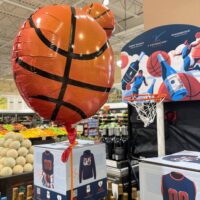 A basketball-shaped balloon in a grocery store next to a display with a basketball hoop and wine.