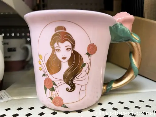 A pink mug with Belle from Beauty on the Beast on it with a rose handle on a shelf in a store.