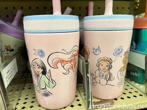 Two pink tumblers with straws on top decorated with Disney Princesses on them on a shelf in a store.