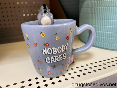 A blue mug with Eeyore from Winnie The Pooh on the top and the words "Nobody Cares" and flowers on it.
