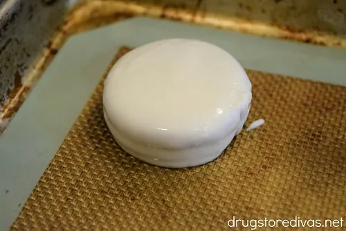 A white chocolate covered Oreo sitting on a silicone baking mat on a cookie sheet.
