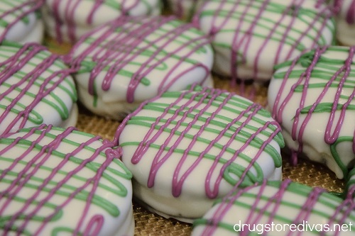Green and purple candy melts drizzled on white chocolate covered Oreo cookies.