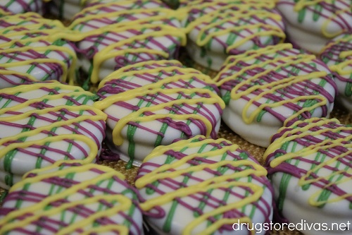 Green, purple, and yellow candy melts drizzled on white chocolate covered Oreo cookies.