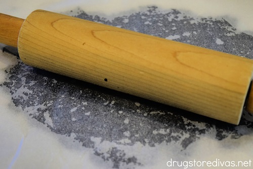 A rolling pin rolling out Oreo cookie crumbles under parchment paper.