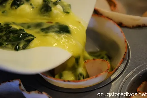 Egg, spinach, and feta cheese mixture being poured from a bowl into turkey-slice lined muffin tin cavities.