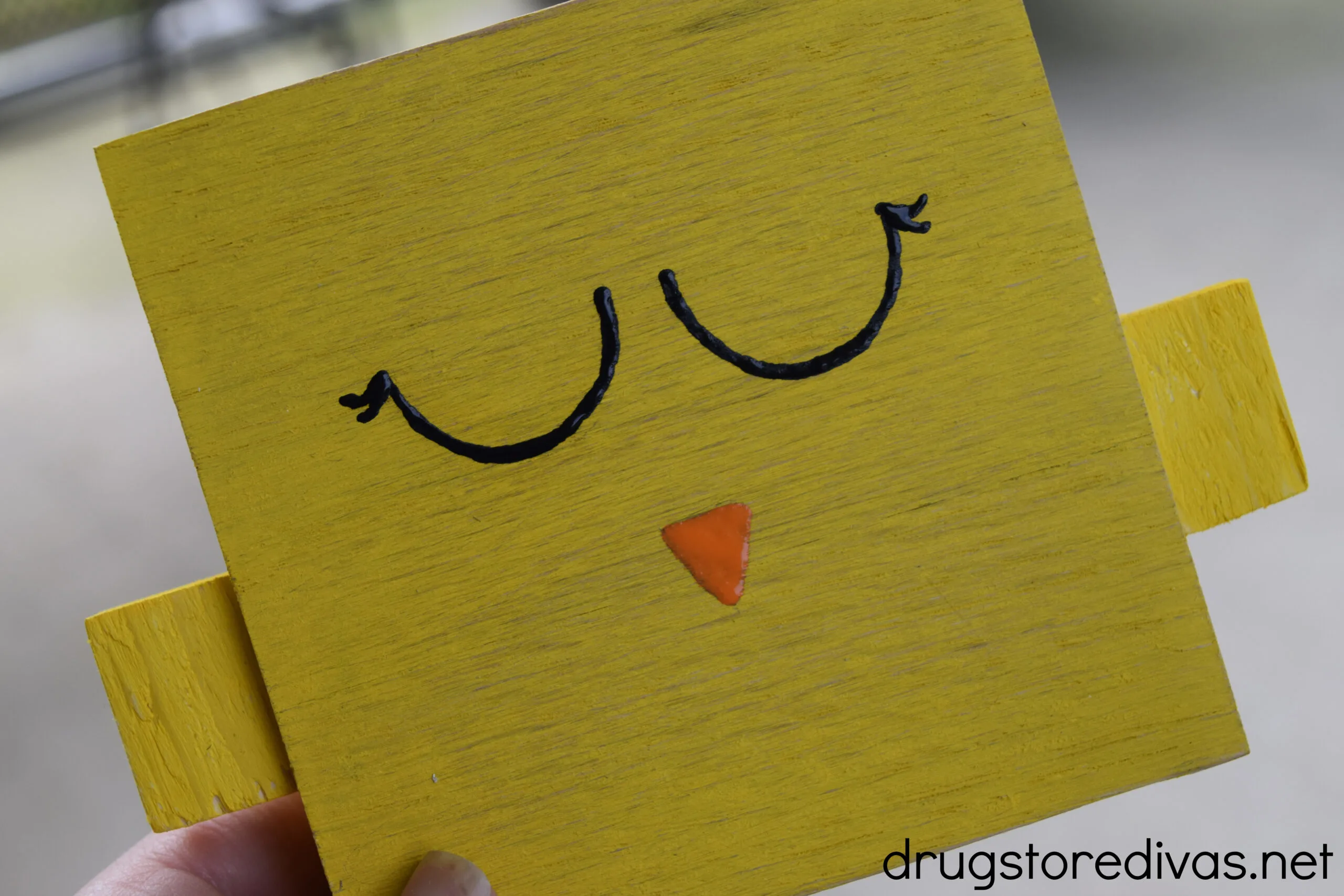 A cartoon chicken face painted on a yellow block of wood.