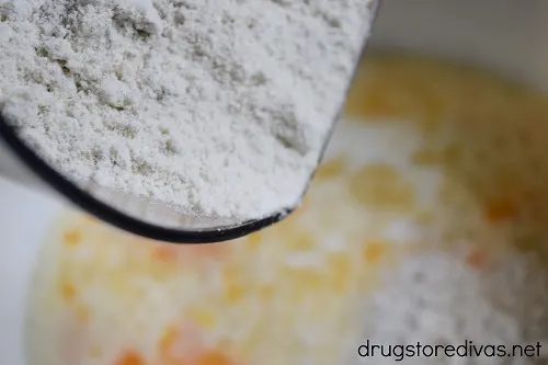 Flour being poured into a bowl that's filled with eggs and milk mixed together.