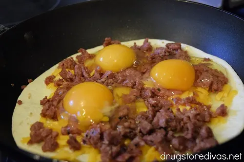 Three eggs on top of sausage on top of cheese on top of a tortilla in a pan.